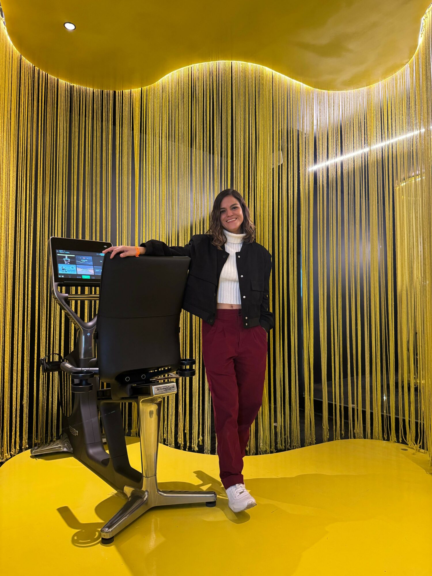 Woman standing in a room with yellow and black striped curtains, a yellow ceiling, and a yellow floor, next to a computer desk.