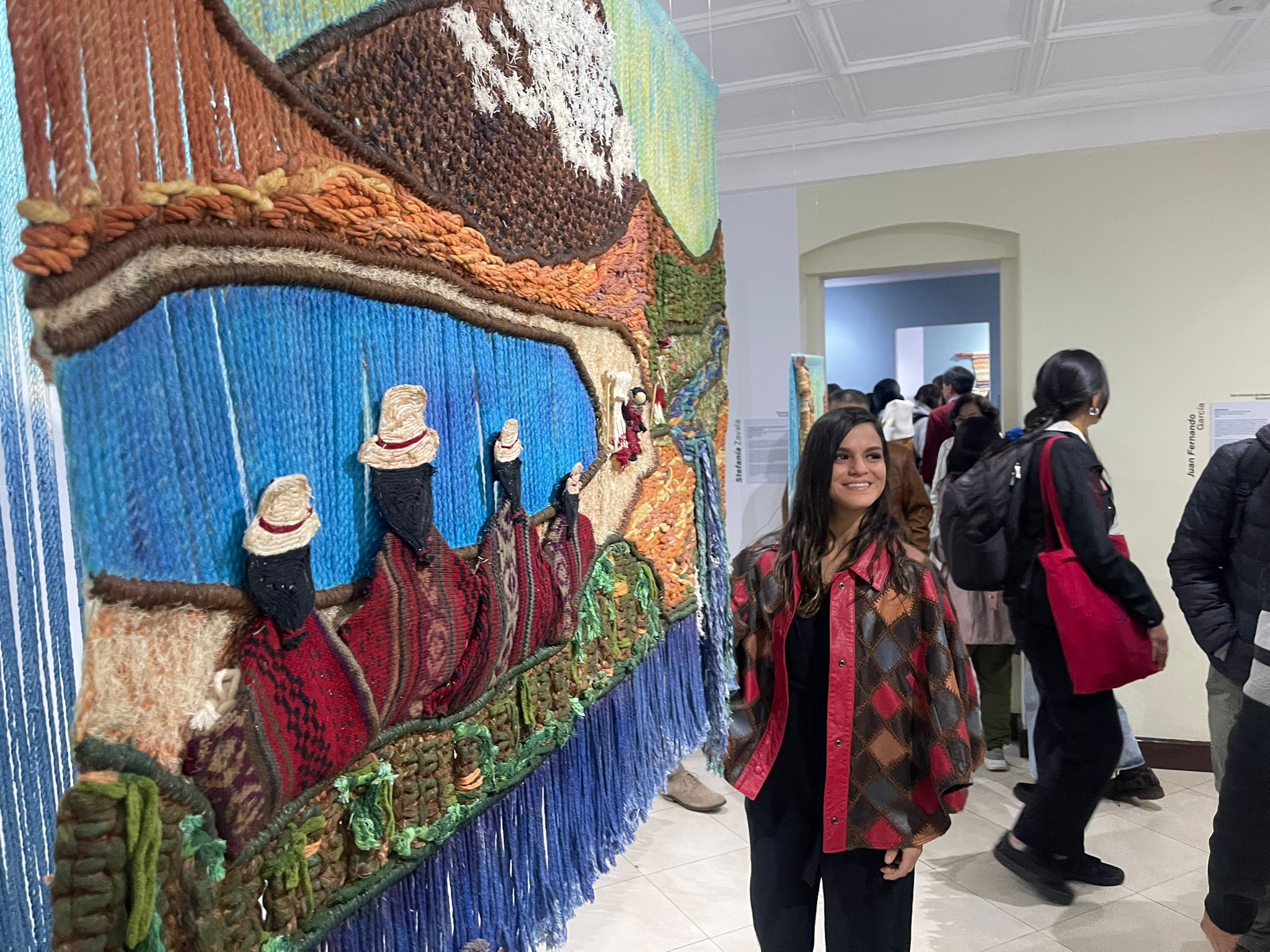 People in a gallery looking at a large textured artwork on the wall, with some individuals walking and observing exhibits.