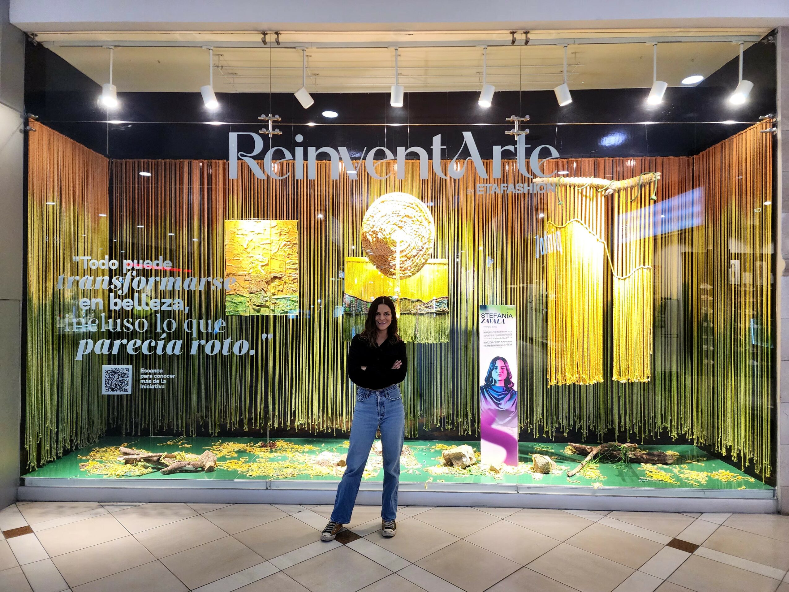 Person standing in front of an art display with colorful hanging strands and illuminated artwork, with text in the background.