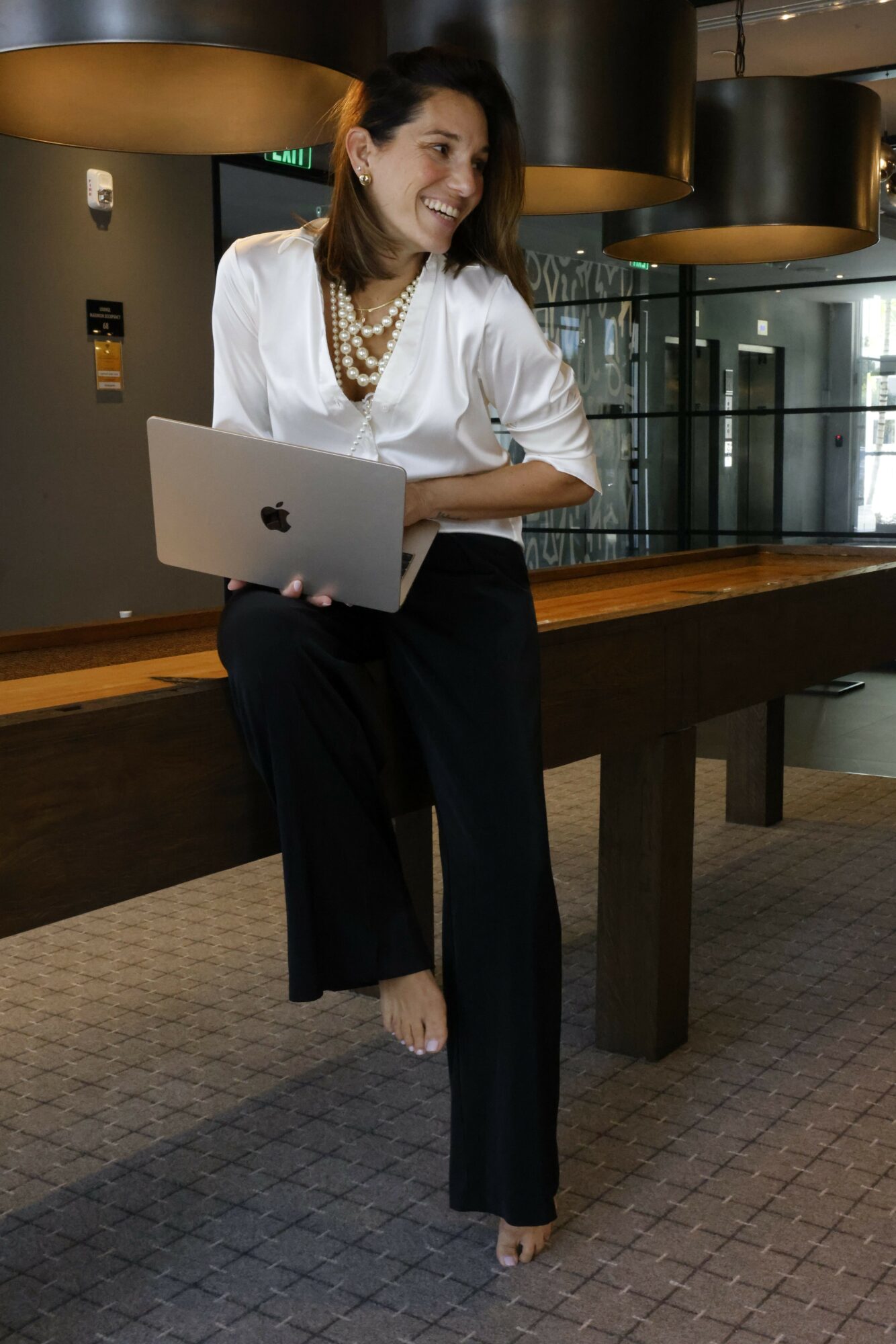 Woman lying on a table with a laptop, resting her head on her hand, in a modern indoor setting.