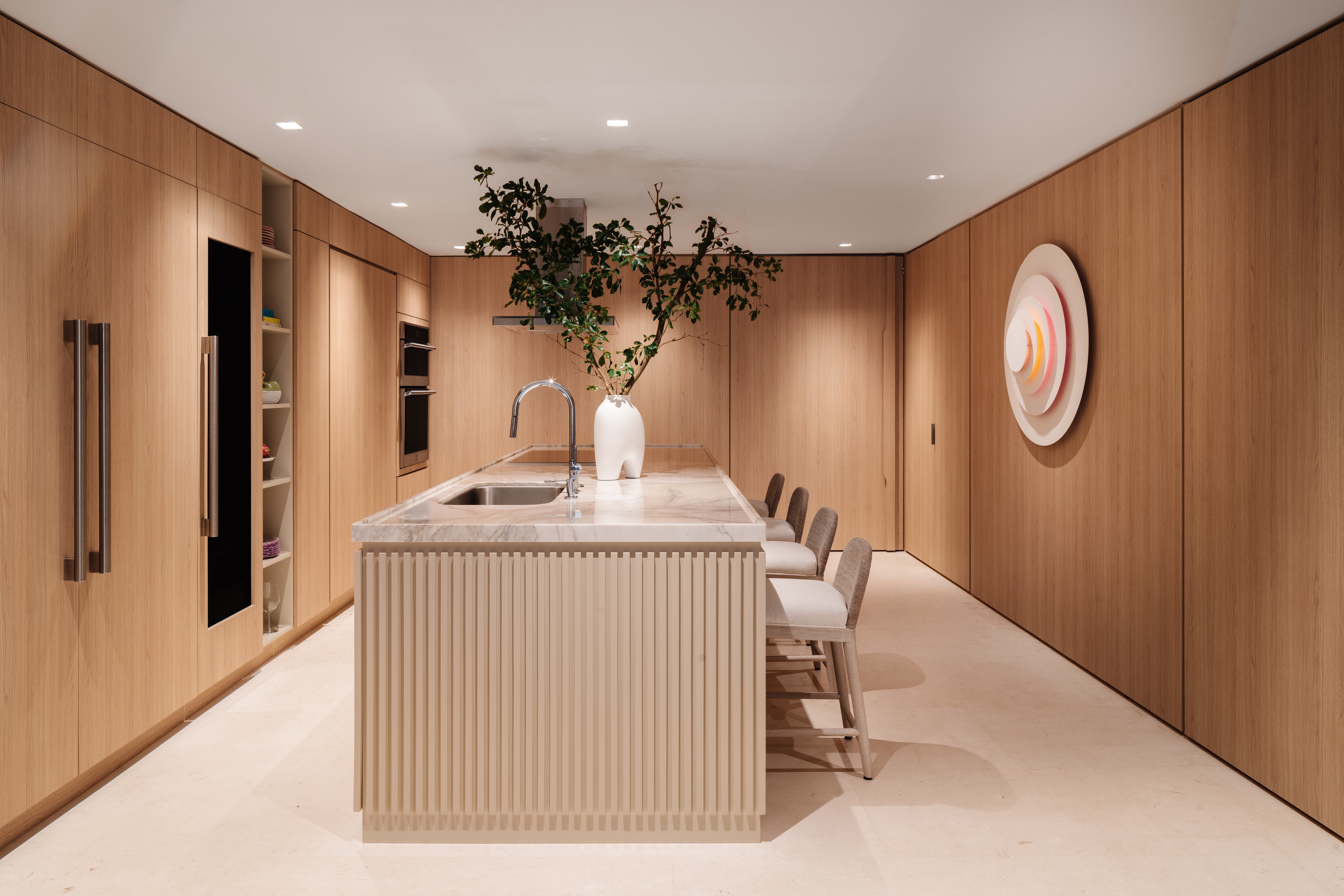 Modern kitchen with wooden walls, a central island with a white vase and plant, and four chairs, minimal decor.