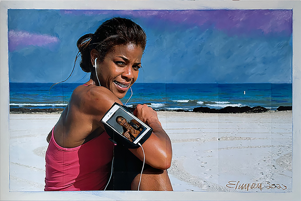 Woman smiling at camera while holding a phone with a beach background, wearing a pink top, hair tied back.